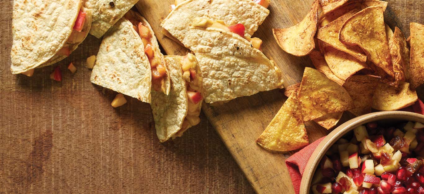 Cinnamon Apple Quesadillas on a wooden cutting board next to a bowl of apple salsa