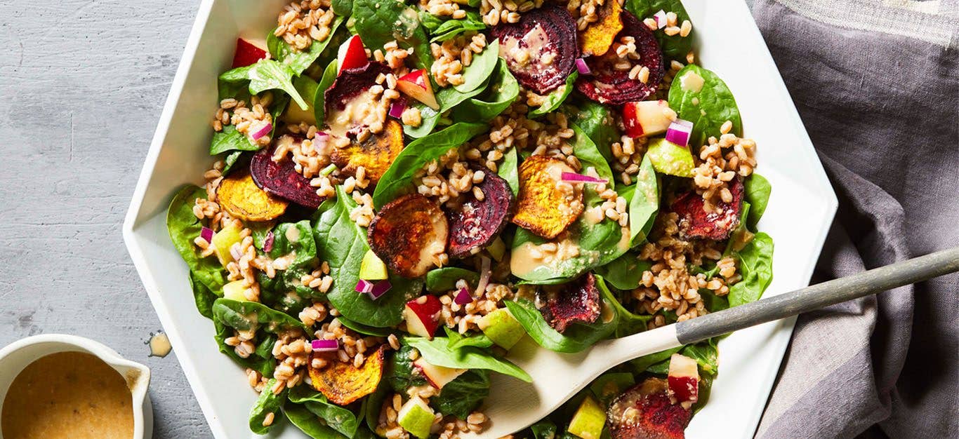 Crispy air fryer beets sit atop a colorful green salad with spinach and other chopped veggies including fresh pair, in a hexagonal white bowl in bright light