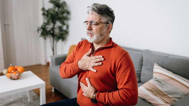 Older man in an orange sweater with a hand on his heart and a hand on his belly, breathing deeply