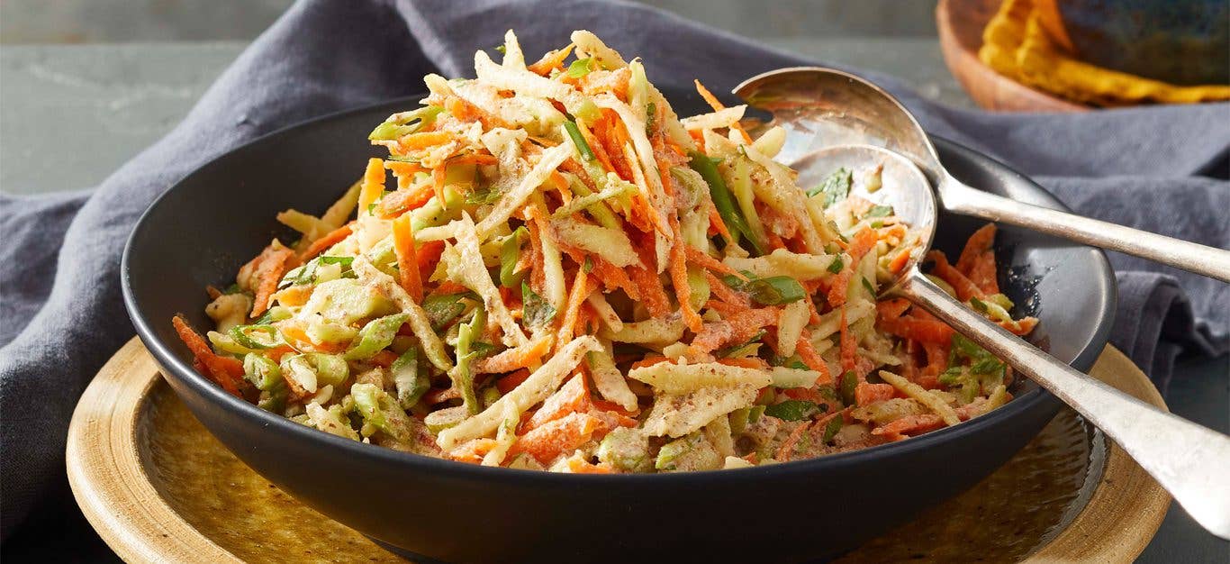 The Best Broccoli Slaw in a black bowl with metal serving spoons