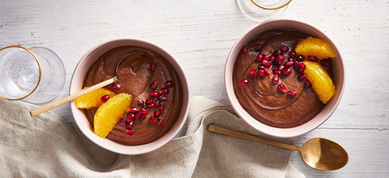 Vegan chocolate avocado pudding in white ramekins sprinkled with pomegranate seeds and orange slices