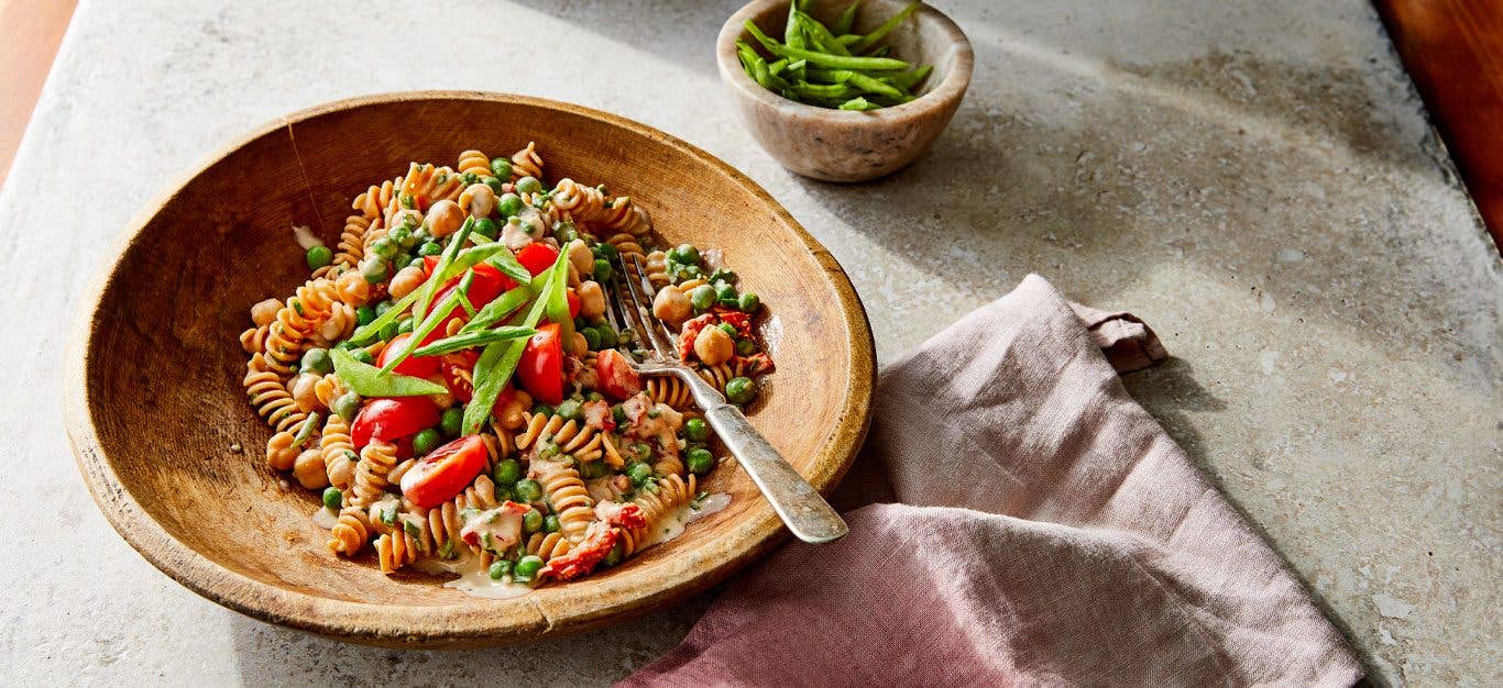 Creamy Chickpea Pasta Primavera in a wooden bowl with a metal fork on a cement countertop