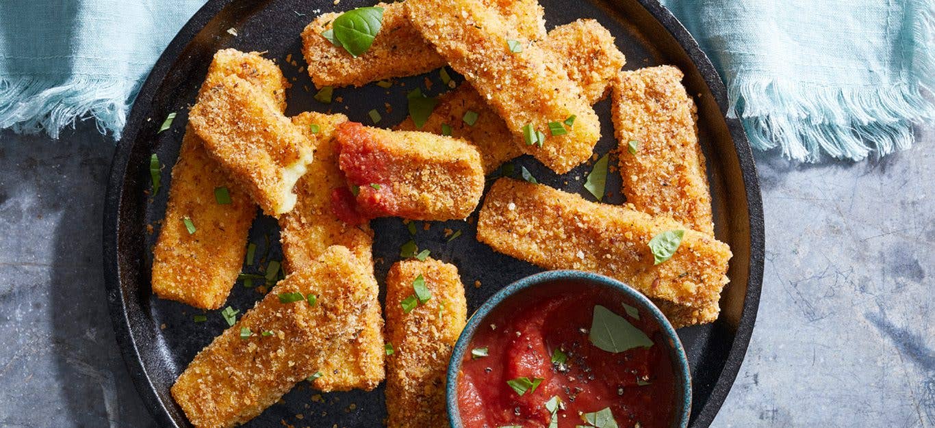 Crispy Potato Vegan Mozzarella Cheese Sticks on a platter with a ramekin of marinara, atop a blue tablecloth