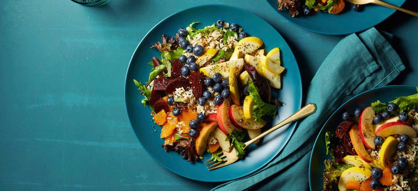 Eat-the-Rainbow Salad on a blue plate with metal fork on a teal tabletop