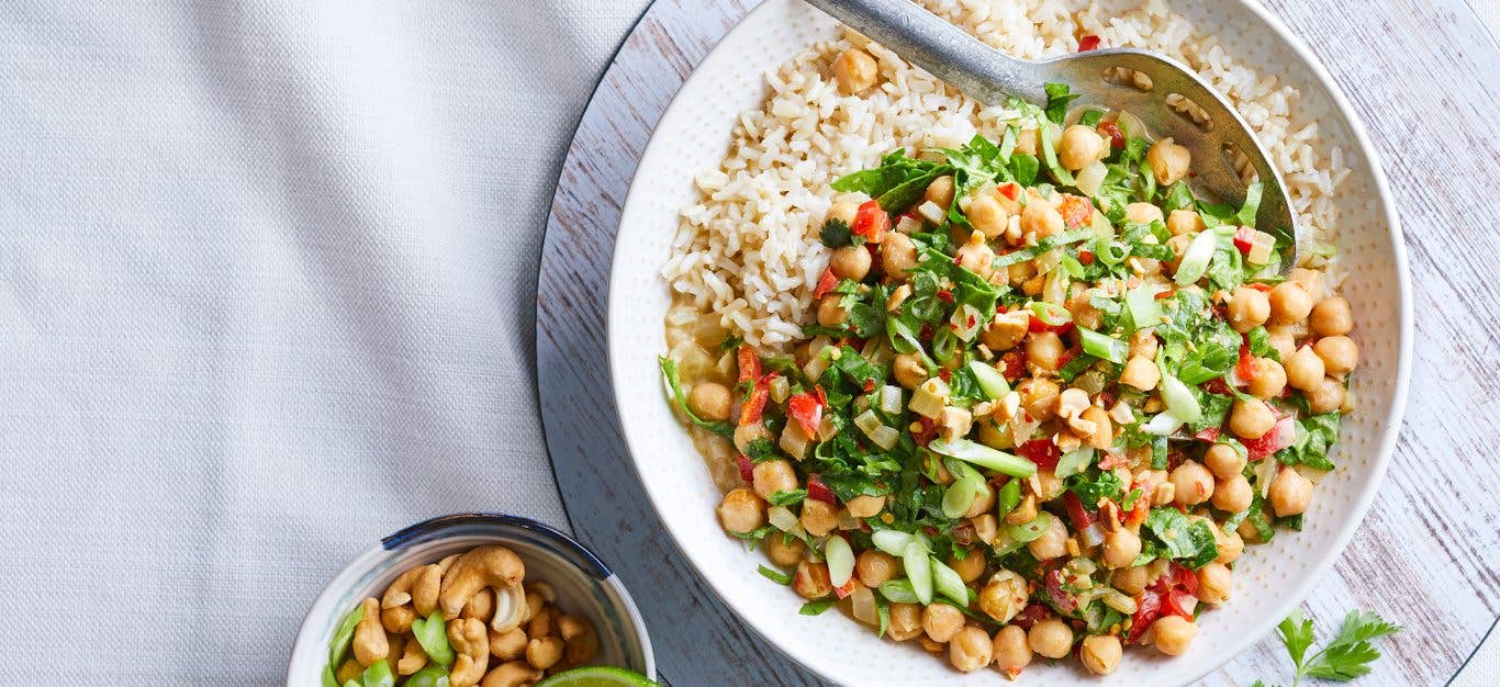 Thai Green Curry Chickpeas with Spinach in a white bowl with a metal serving spoon