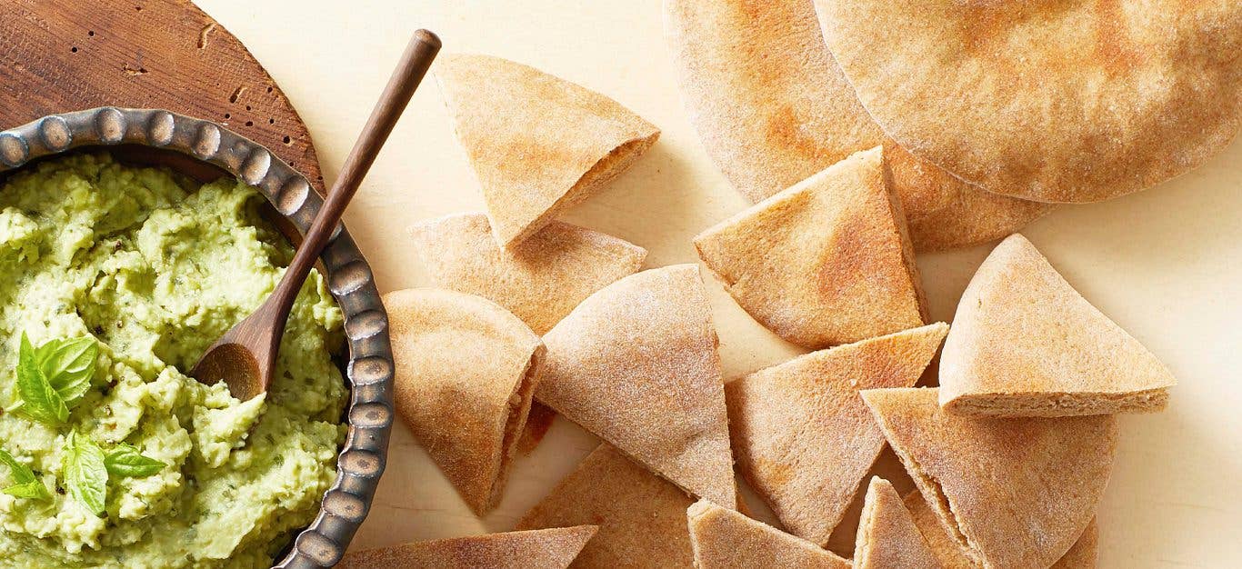 Homemade Vegan Pita Bread cut into triangles on a white counter next to a bowl of green hummus