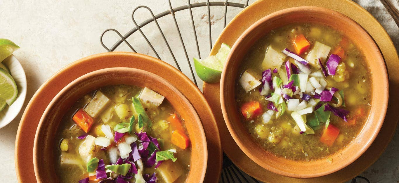 Jackfruit Pozole Verde in orange terracotta bowls with lime wedges on the side