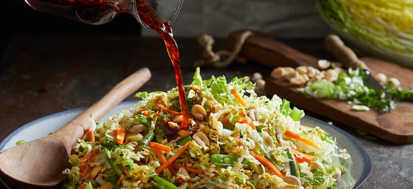 Napa Cabbage Salad on a serving plate with dressing being poured over the top