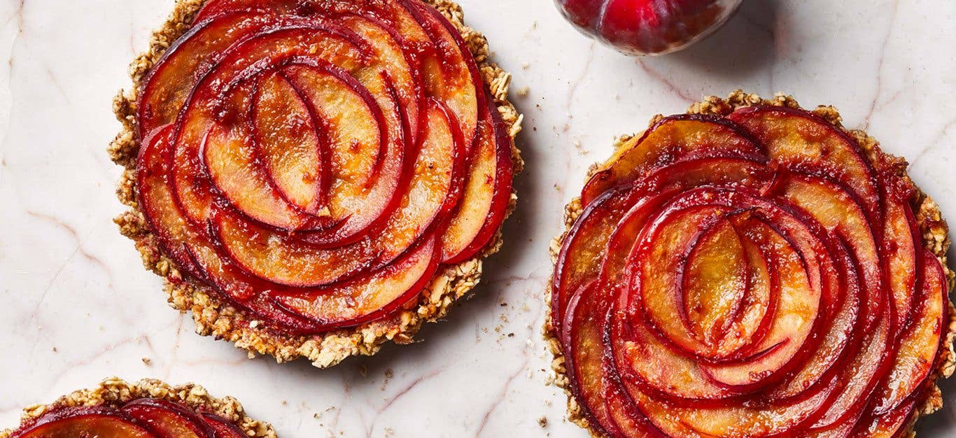 Two pretty pink-red rosette plum tarts side by side on a light marble table