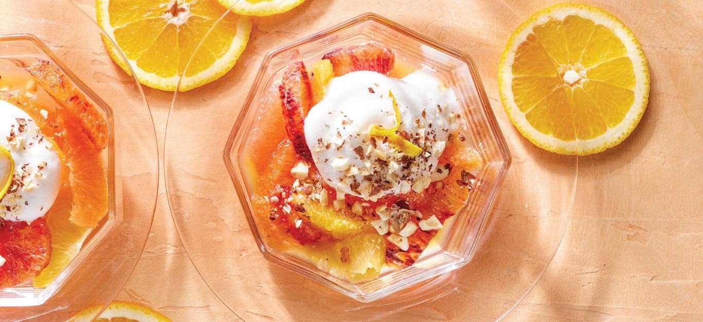 Poached Citrus with Aquafaba Whipped Cream in a cocktail glass on a peach colored background