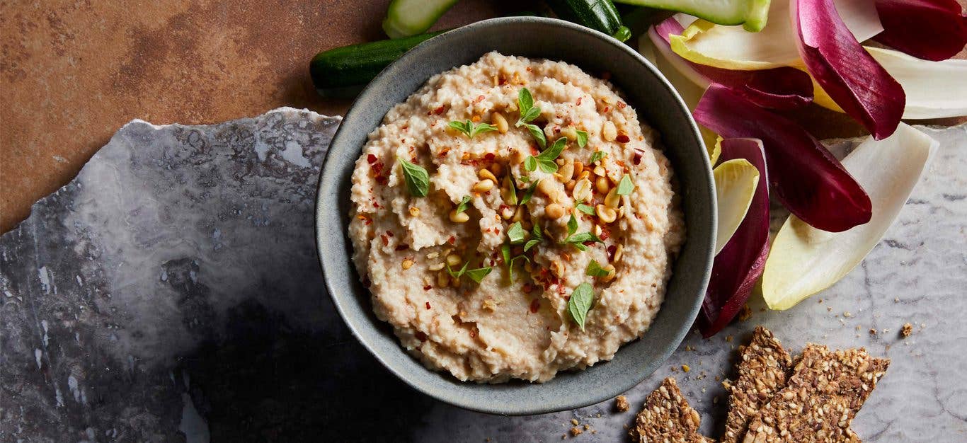 Roasted Cauliflower Hummus in a gray bowl surrounded by crackers and endive leaves