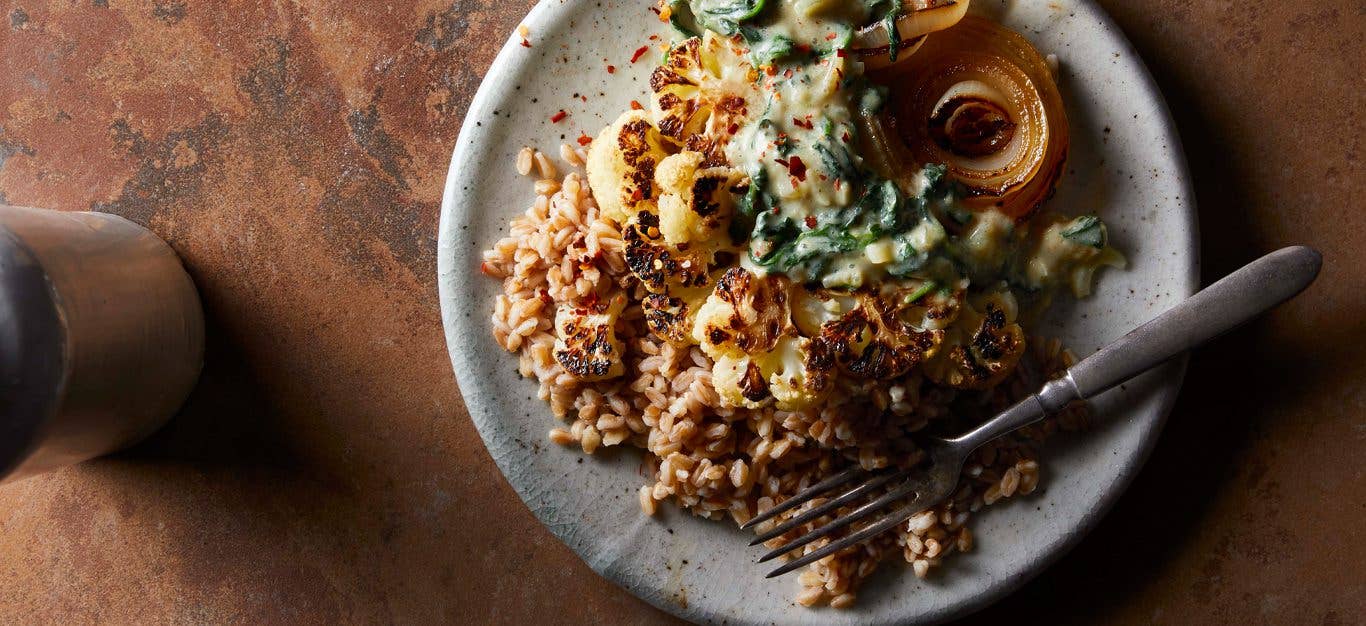 Roasted Cauliflower Steaks with Creamed Spinach on a white plate with a metal fork