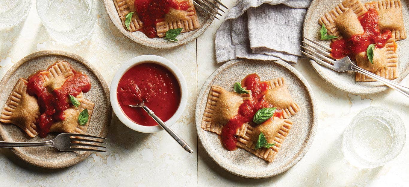 Kale and Sweet Potato–Stuffed Vegan Ravioli on gray ceramic plates topped with marinara sauce and fresh basil