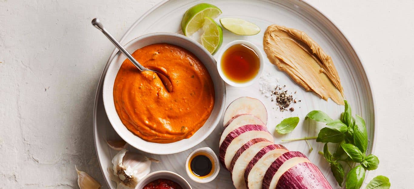 Light Thai Peanut Dressing in a white bowl surrounded by eggplant, soy sauce, peanut butter, and lime slices