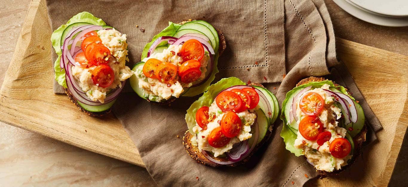 White Bean Toasts with Veggies on a brown cloth napkin resting on a wood cutting board