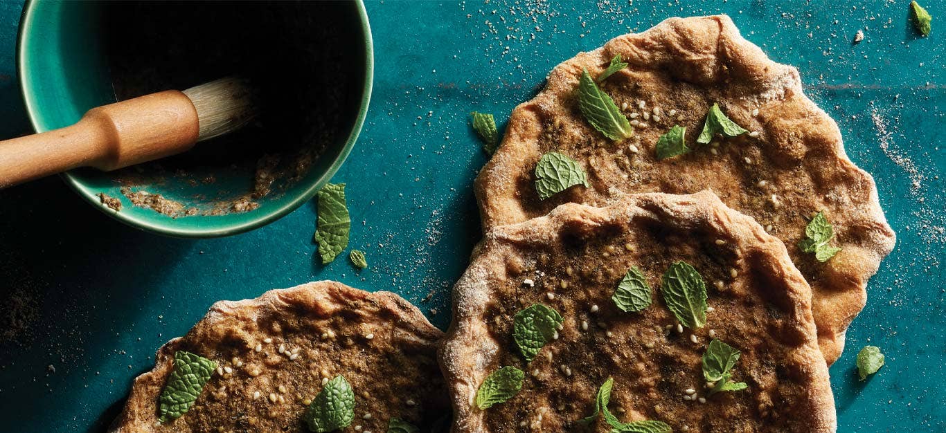 Za’atar-Spiced Flatbreads (Manakeesh) on a blue tabletop next to a bowl za'atar spice