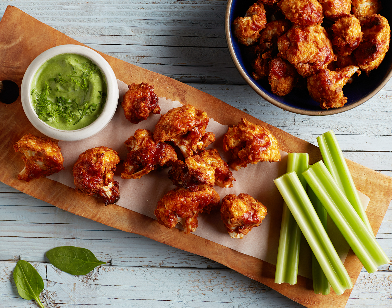 Buffalo cauliflower wings shown on a wooden serving board with sauce and celery sticks, a vegan recipe